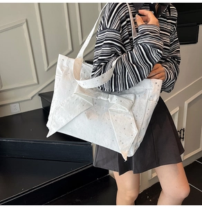 Close-up of white canvas tote bag with silver star prints and a large decorative bow