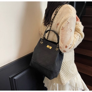 Detailed view of black quilted bucket bag with gold chain strap on wooden stairs