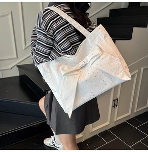 White canvas tote bag featuring silver stars and a large bow shown on a shoulder