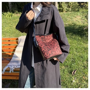 Outdoor shot of a red-brown leopard print bucket bag with black trim on a green lawn