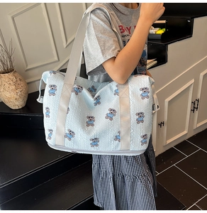 Detail of light blue foldable travel bag with teddy bear pattern and wide shoulder strap