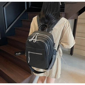 Detailed view of black pebbled leather backpack featuring multiple silver zippers and side strap