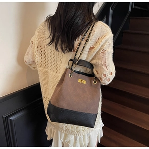 Close-up of quilted bucket bag with chain strap and gold lock worn by a model