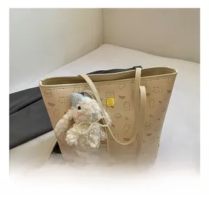 Close-up of cream tote bag featuring cartoon bear prints and plush rabbit charm accessory