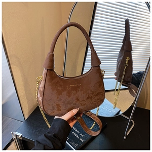 Détail du sac croissant en daim marron avec bandoulière chaîne dorée et logo embossé