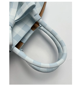 Détail d'un sac seau à carreaux bleus montrant un nœud décoratif, une anse et un bord en cuir