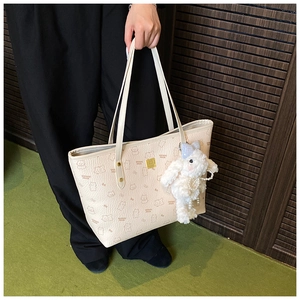 Detail of beige tote bag with bear print, gold logo, and plush bunny charm accessory