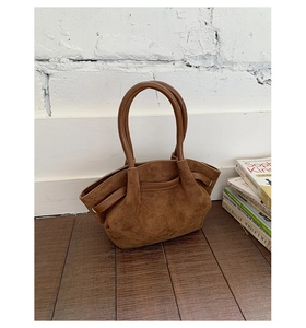 Detail of vintage brown suede tote bag with pleated sides and round handles on wood floor