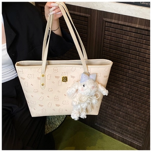 Detail of beige tote bag featuring cartoon bear patterns and a plush bunny charm