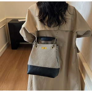 Detail of quilted bucket bag featuring a gold chain strap and smooth metal turn-lock