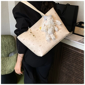 Detail of beige tote bag with bear print featuring a plush rabbit charm and pearl accent