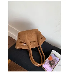 Detail of a brown suede tote bag featuring smooth cylindrical leather handles and texture