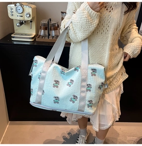Detail of light blue quilted travel bag featuring cute bear embroidery and gray handles