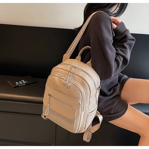 Beige lychee texture backpack with printed straps shown on model in a modern indoor setting
