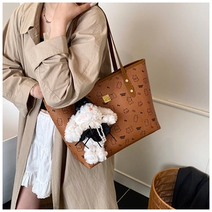 Brown leather tote bag with cartoon bear pattern and plush rabbit pendant detail