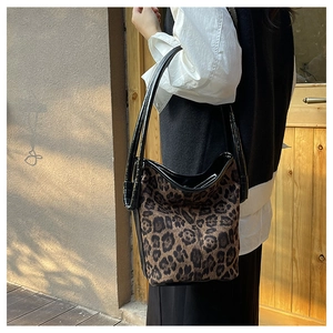 Detail of leopard print bucket bag with glossy black straps against stone wall