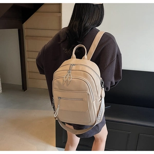 Rear view of a model wearing the beige leather backpack with a decorative jacquard strap