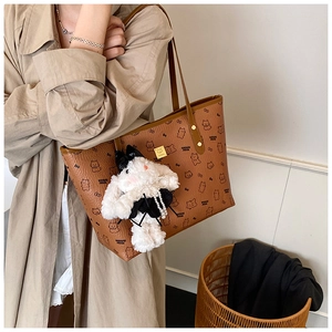 Brown litchi grain tote bag with bear patterns and a plush rabbit charm on a model