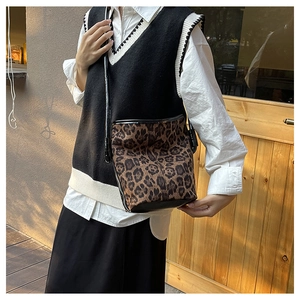 Leopard print bucket bag with black leather trim shown on shoulder in outdoor setting