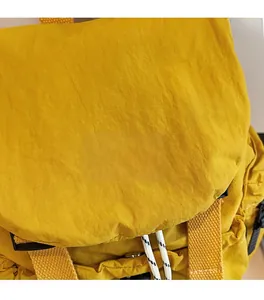 Détail de la texture du tissu en nylon jaune et logo de la marque sur le sac à rabat