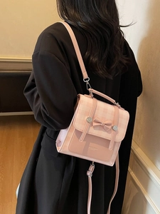 Pink plaid backpack with bow accent worn by model in a minimalist indoor setting