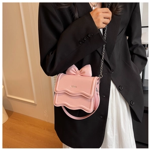 Close-up of pink mini crossbody bag with 3D bow and wavy edge on a chic model