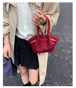 Detail of burgundy suede tote bag with smooth leather handles in an outdoor setting