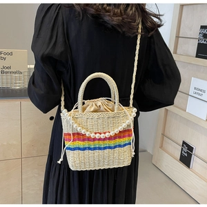 Detail of straw bucket bag featuring rainbow stripes, pearl handle, and drawstring closure