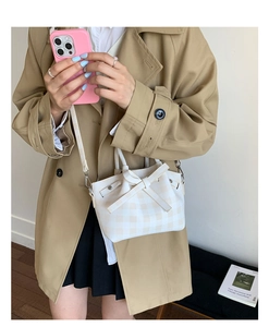 Détail d'un mini sac seau à carreaux beige avec un nœud, porté par un mannequin en trench-coat