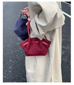Close-up of a burgundy suede tote bag held by a person wearing a beige trench coat