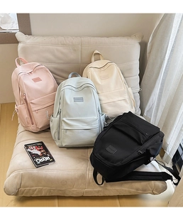 Multiple casual nylon backpacks in pink, white, blue, and black displayed on a sofa