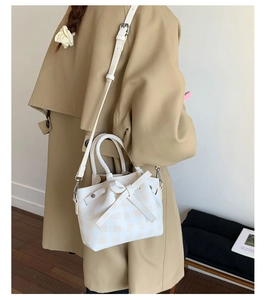 Détail du sac seau à carreaux avec un nœud décoratif et une bandoulière réglable