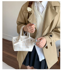 Détail du sac à damier crème avec nœud porté par un mannequin en trench-coat élégant