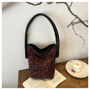 Detail of leopard print bucket bag with black glossy handle on a wooden table setup