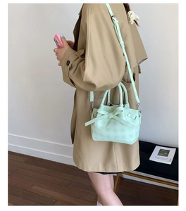 Détail du sac seau à carreaux vert menthe avec nœud porté avec un trench-coat kaki classique