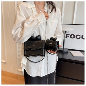 Detail shot of mini black crossbody bag with bow accent and chain strap on a white shirt