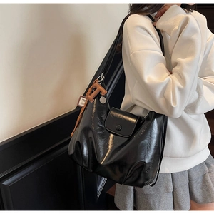 Detail of glossy black leather tote bag featuring a decorative orange H letter pendant