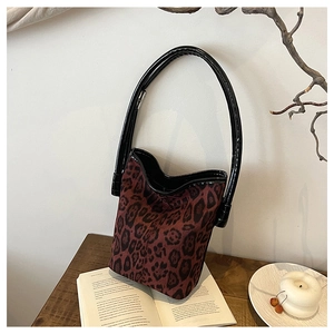 Detail of leopard print bucket bag with black glossy handle on a wooden table