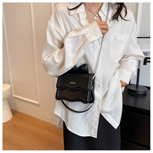 Mini black crossbody bag with wavy flap, bow decoration, and chain strap on a model