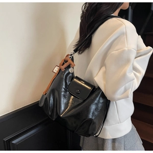 Close-up of black glossy leather shoulder bag featuring front pocket and H letter charm