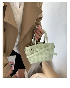 Détail du sac cabas à carreaux vert clair avec nœud porté sur un trench-coat beige