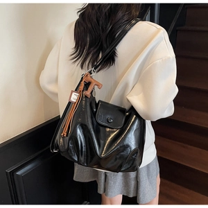 Detail of glossy black shoulder bag with brown tassels and leather texture finish