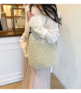 Detail showing handwoven texture of beige straw shoulder bag with dark leather strap