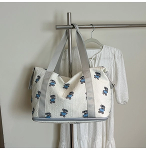 Detail of white quilted travel bag featuring blue bear embroidery and separate shoe compartment