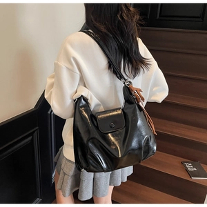 Detail of glossy black hobo bag with flap closure and brown fringe tassel accent