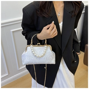 Close-up of white jacquard fabric with pearl handle and golden chain on shell bag