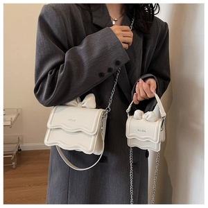Close-up of cream white bow bags with wavy edges and metal chains on grey blazer