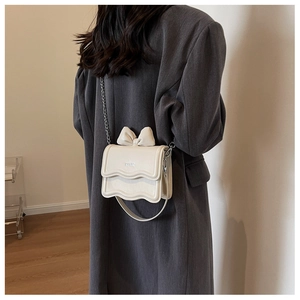 Close-up of cream PU leather crossbody bag with bow decoration on a gray coat