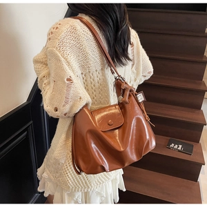 Brown soft leather tote bag with flap closure shown on model in stylish indoor setting