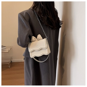 Detail of cream crossbody bag with bow accent and chain strap worn over a grey blazer